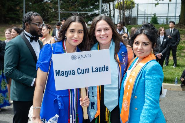 Honors graduates smile and hold up a Magna Cum Laude sign, as they wait for the convocation to begin