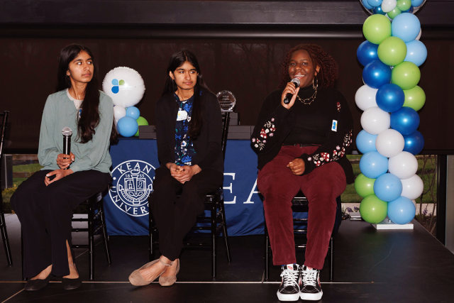 Three females students sit on a stage, each with a microphone. Oluwatunmise Alabi, on the right, is speaking.