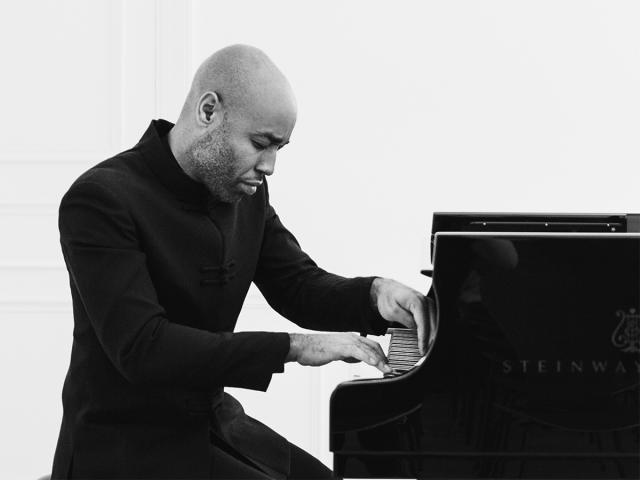 Aaron in a black and white photo, playing the piano. His gaze is focused on the keyboard
