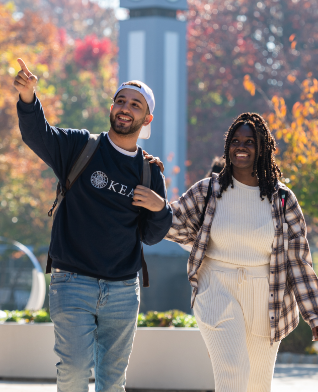 Two students, one in Kean sweatshirt, walking together outside on Kean campus on a fall day