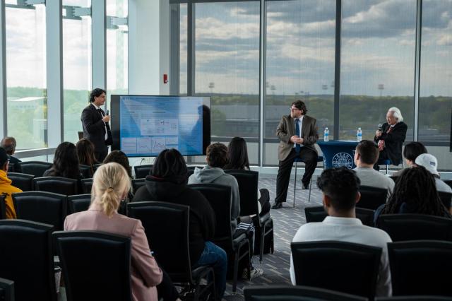 Eric Landaverde presents his research to physicist Michio Kaku before a room of students.