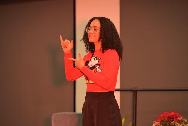 Lauren Ridloff signs in ASL, wearing a red sweater