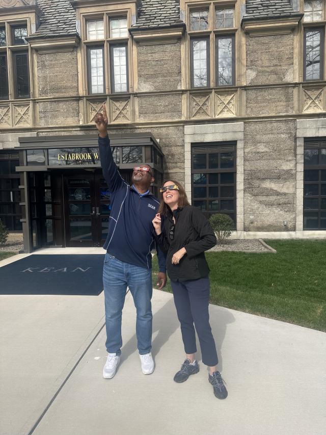 Kean President Repollet, wearing eclipse sunglasses, points to the sky as he stands next to VP Karen Smith