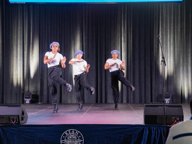 Students in white t shirts, black pants and blue berets perform a step routine.