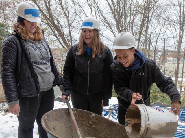 Three students mix the stucco in a wheelbarrow 