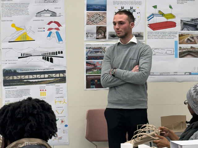 Sean Santos is presenting in an architecture class. Posters are behind him.