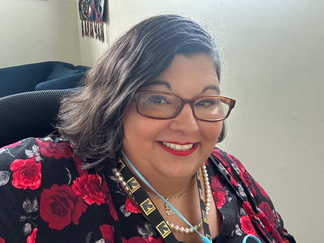 Tina-Marie Lopez, a Hispanic woman with shoulder-length dark hair and rectangular glasses, wearing a bright floral print shirt