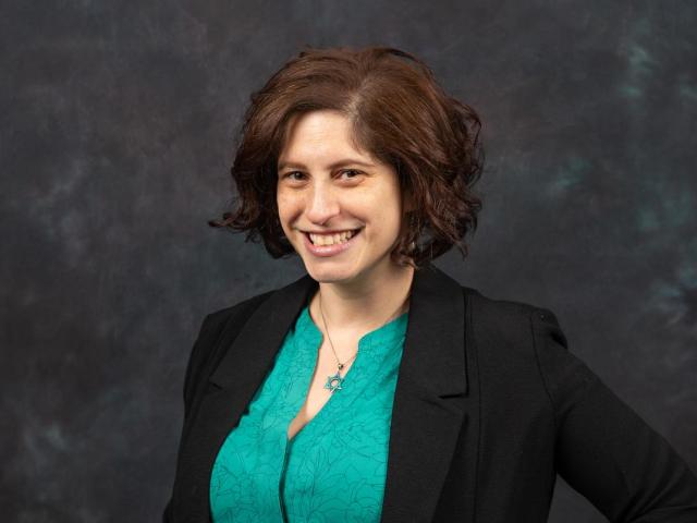 Dr. Adara Goldberg, a Jewish woman with short brown hair, green blouse, black jacket, smiling.