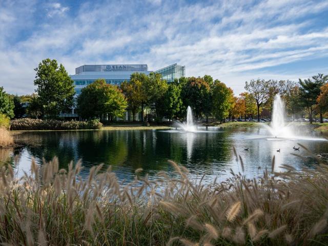 A pond with a fountain on Kean's campus. In the distance, is Kean's STEM Building