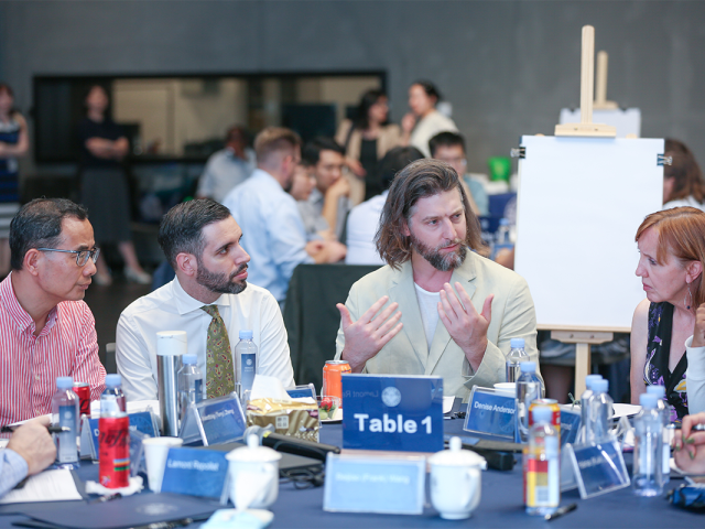 Three men and a woman sit at a table, having a discussion.