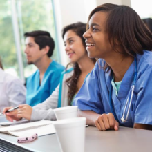 Three students in medical scrubs seated at a long table