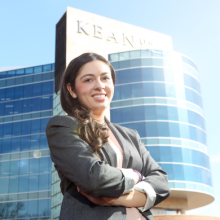 Student with arms crossed standing in front of Kean business school building