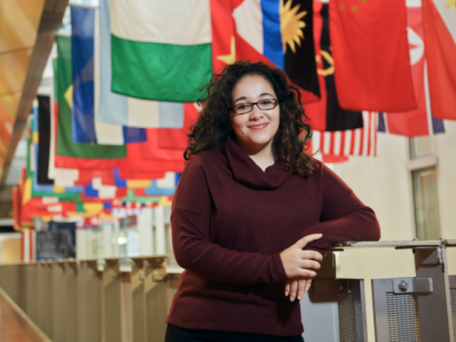 Woman standing at the front of a hall where many international flags hang from the ceiling