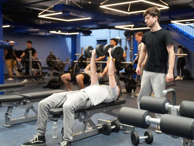 Students at a Kean fitness center, one spotting while the other lifts weights