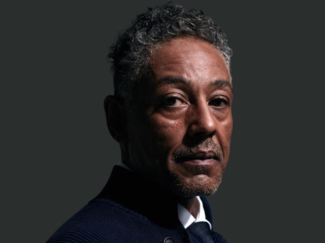 Portrait of Giancarlo Esposito, actor known for his roles in 'Breaking Bad' and 'The Mandalorian,' wearing a dark textured jacket over a white shirt. He has short, curly grey hair and a trimmed goatee, with a contemplative expression as he looks slightly off to the side. 