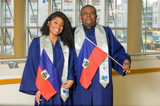 Daughter and father graduates, Welena (L) and Wisner Noel, proudly display the Haitian flag. The family has proud Haitian roots.