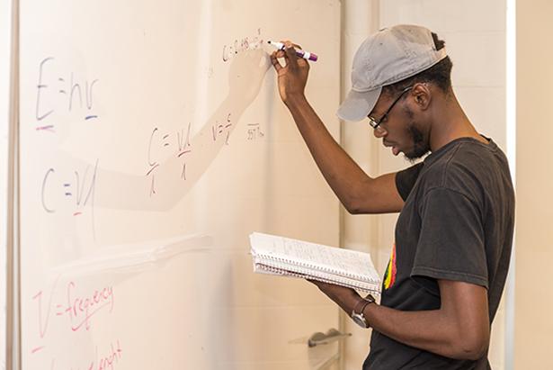 A Kean student works at a whiteboard.