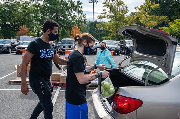 Kean students volunteering at a food distribution event load produce into the trunk of a car.