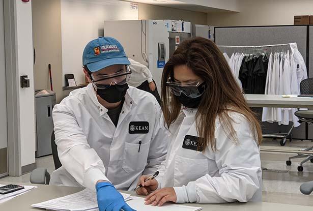 Two workers at Kean's COVID-19 lab collaborate as they review paperwork.