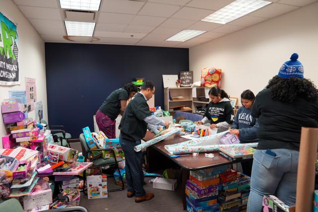 A room filled with children's toys, and a table with volunteers wrapping holiday gifts.