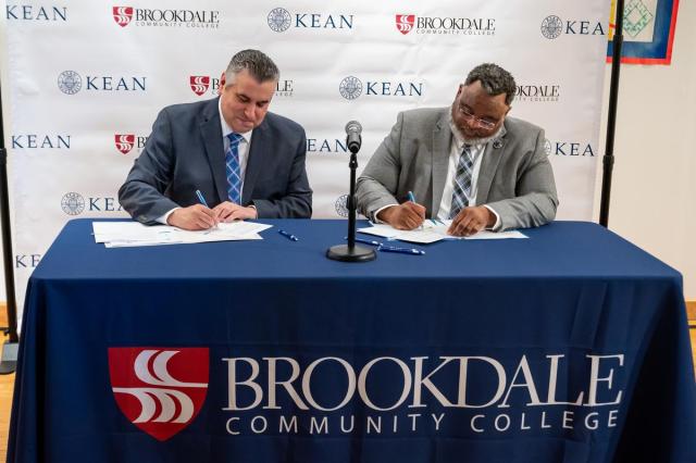 At a desk with a Brookdale sign, President Stout and President Repollet sign documents.