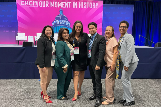 A group of Kean administrators, with a student, pose before a CHCI Our Moment in History sign.