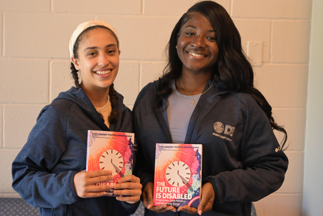 Two female students stand together, holding The Future Is Disabled