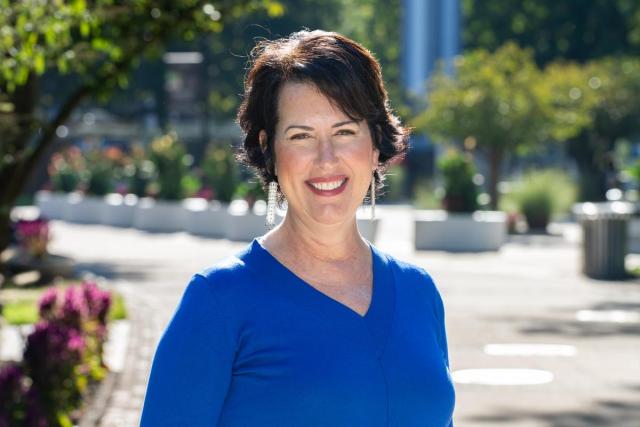 Laura Baecher in a blue shirt smiles as she stands on Kean's Union campus.