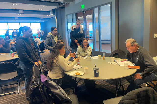 A group of female Kean students in a discussion with a man around a table.