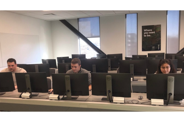 Three students work on separate computer monitors.