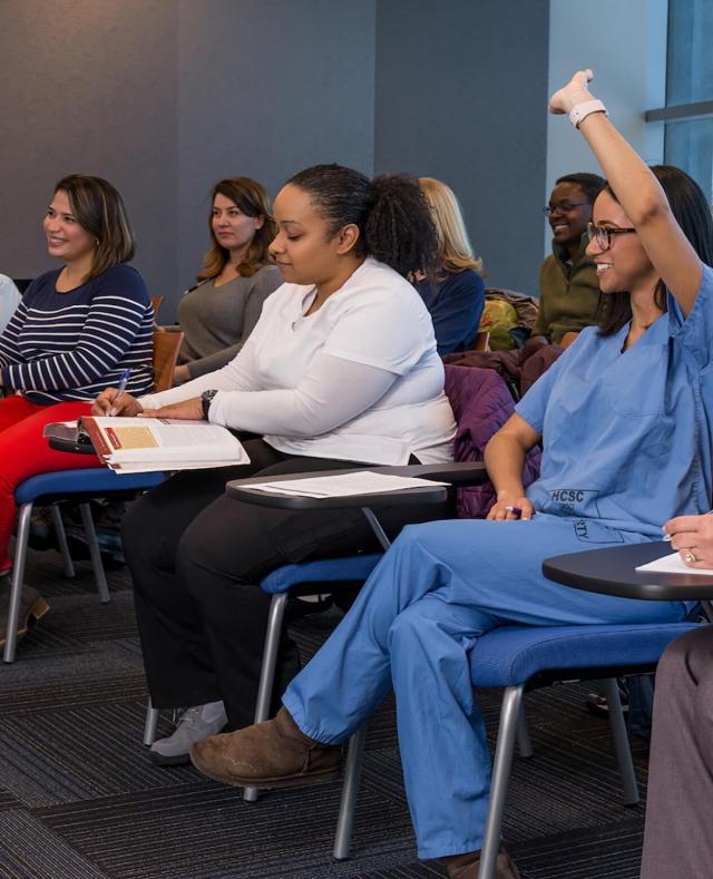 Classroom with students, one of whom is in scrubs and raising her hand