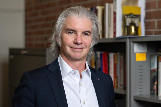 Jonathan Mercantini stands in front of a bookcase and a brick wall