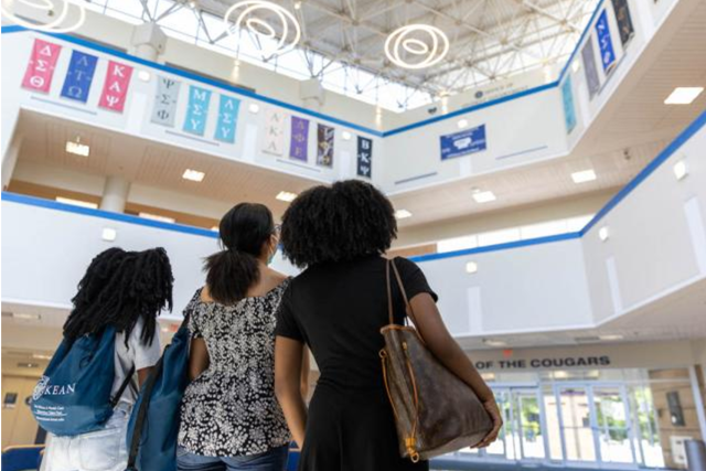 Three young women, one with a Kean backpack, stare up at the ceiling through a skylight.