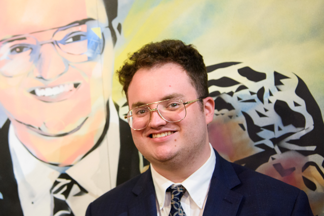 Aidan Allman-Cooper poses in front of his likeness in a mural at Kean