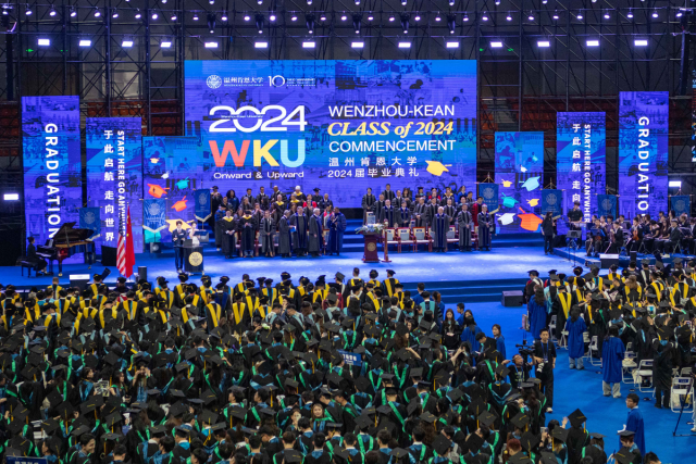An overview photo of WKU's 2024 commencement, with students in caps and gowns, a stage of dignitaries and a sign reading WKU Class of 2024