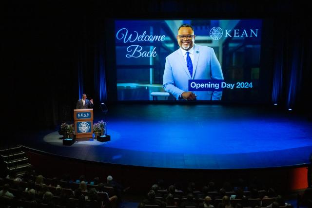 President Repollet picture is on large screen behind, and he is at podium