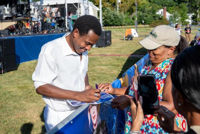 Musician Solomon Hicks, dressed in white, smiles as he signs autographs for a fan.