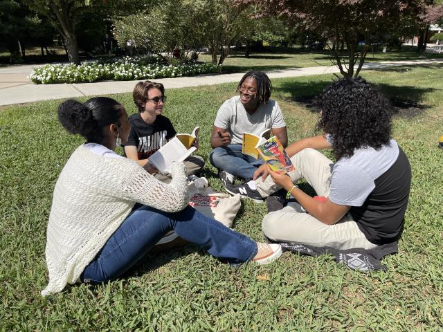 A diverse group of Kean students sits on the lawn, discussing the Common Read book selection