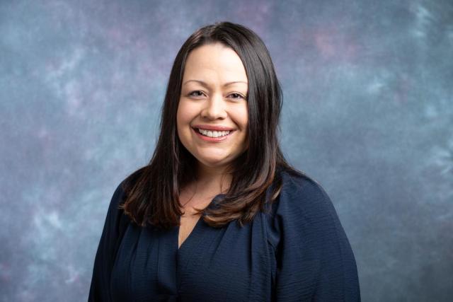 Neva Lozada Headshot - a Latino woman will long brown hair in a navy blue blouse smiles