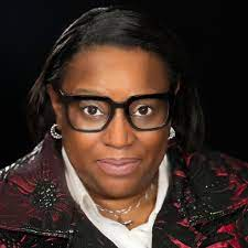 Rev. Pamela Holmes wearing black glasses, earrings and red jacket, with a white shirt. 