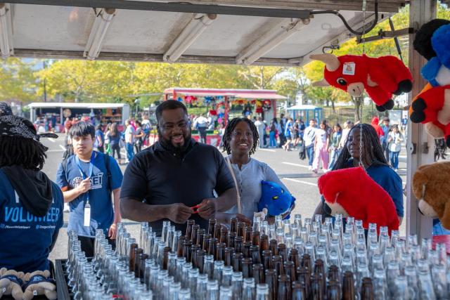 A man stands at a carnival game, ready to throw a ring around bottles.