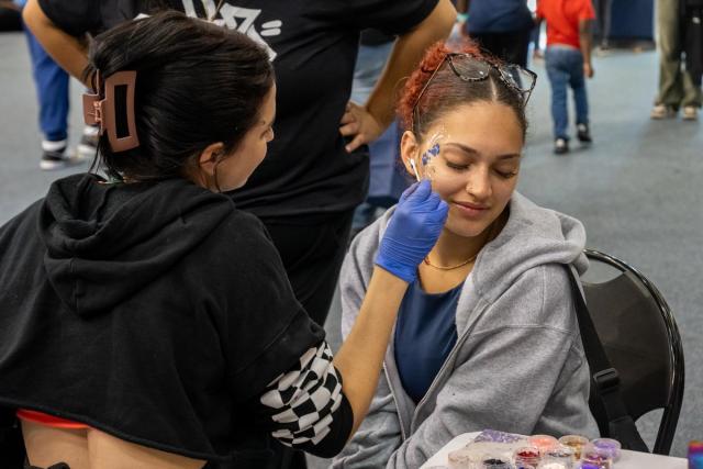 A young woman looks down to the side as her face is painted.