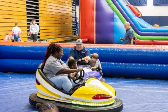 A black woman and her child on a bumper car and next to her a white man and his child on a bumper car