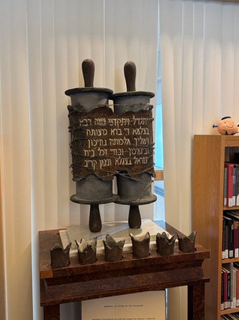 Image of Holocaust memorial: the Torah with the Kaddish, the mourning prayer, wrapped around it as well as barbed wire while at its base is fire representing the way victims of the Holocaust were killed.