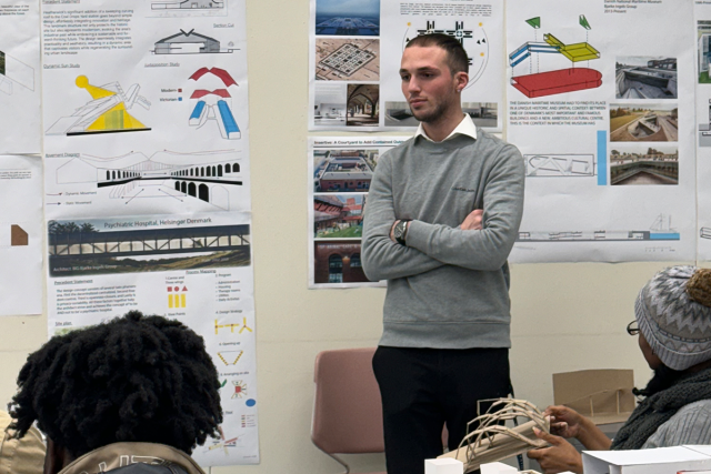 Sean Santos is presenting in an architecture class. Posters are behind him.