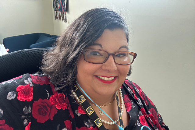 Tina-Marie Lopez, a Hispanic woman with shoulder-length dark hair and rectangular glasses, wearing a bright floral print shirt