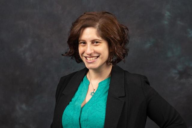 Dr. Adara Goldberg, a Jewish woman with short brown hair, green blouse, black jacket, smiling.