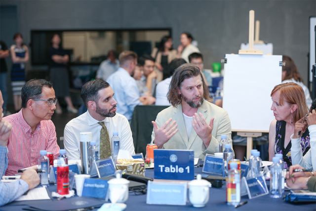 Three men and a woman sit at a table, having a discussion.