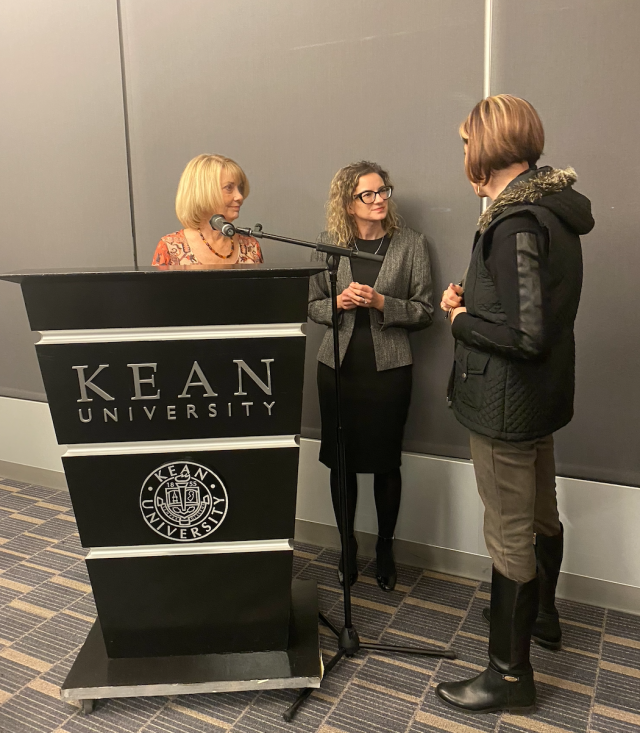 Dr. Sliwa and Dr. White talking with attendee teacher in front of a Kean podium